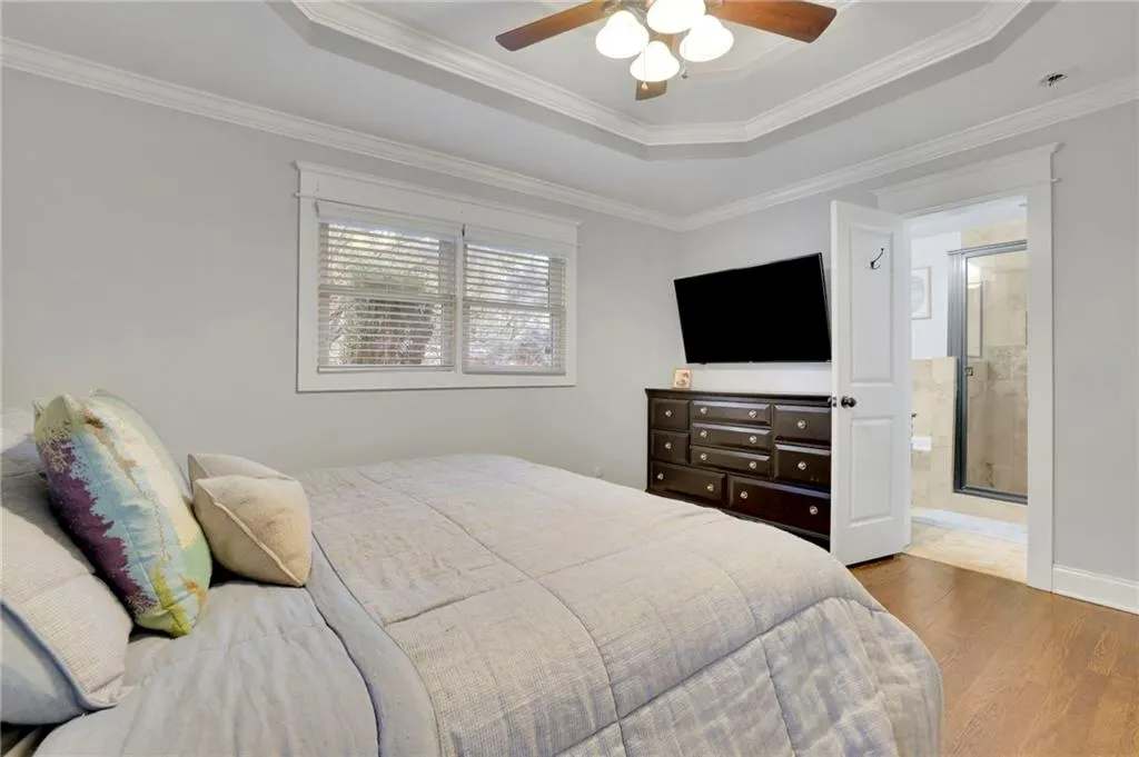 Bedroom featuring hardwood / wood-style floors, ceiling fan, crown molding, and a tray ceiling