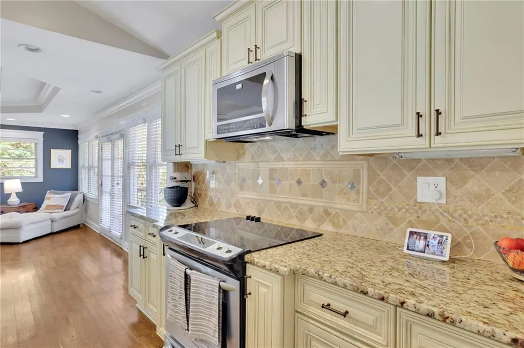 Kitchen with light hardwood / wood-style floors, cream cabinetry, decorative backsplash, appliances with stainless steel finishes, and ornamental molding