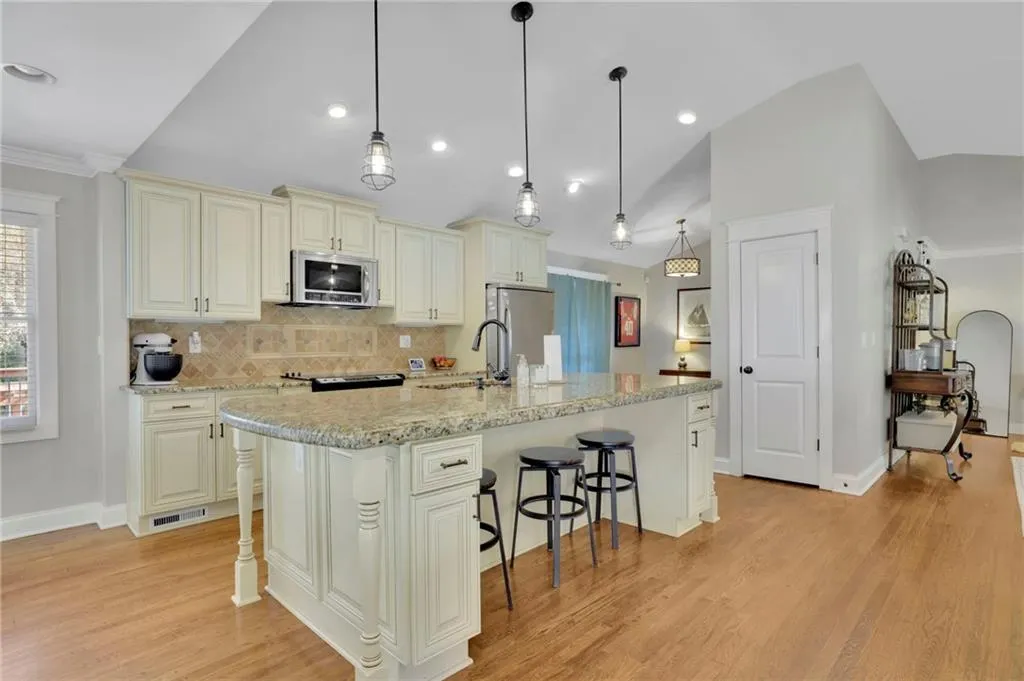 Kitchen featuring a kitchen island with sink, hanging light fixtures, light hardwood / wood-style floors, light stone counters, and stainless steel appliances