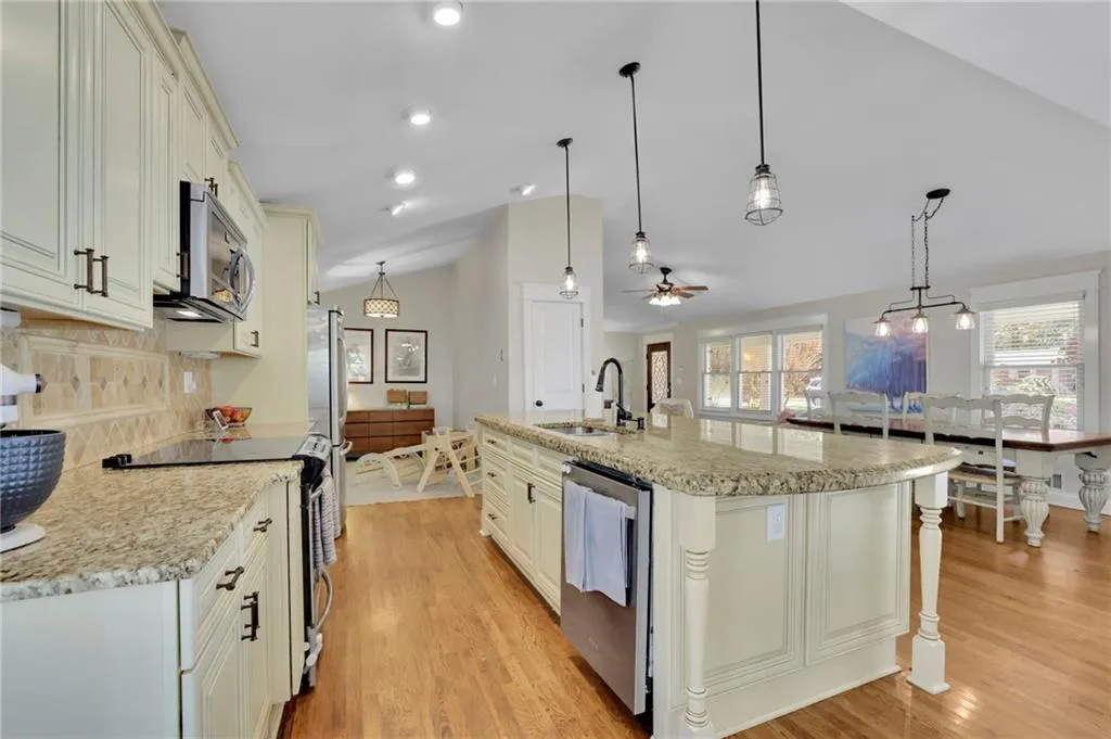 Kitchen featuring lofted ceiling, a kitchen island with sink, sink, appliances with stainless steel finishes, and decorative light fixtures