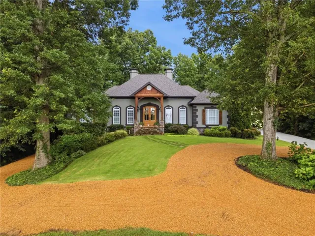 Stucco exterior with stone accents, a prominent wooden entry porch, and a gravel driveway