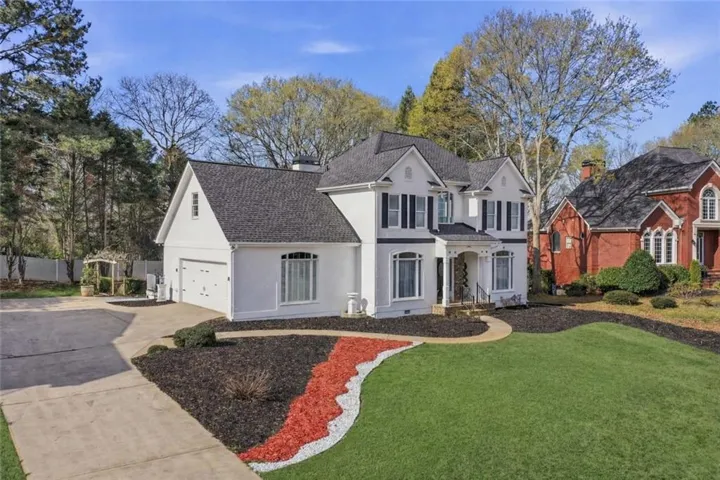 Two-story residence featuring a white stucco exterior with black window shutters and a dark shingle roof