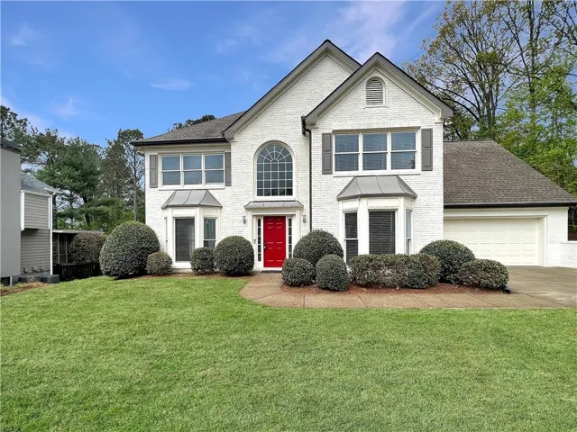 Two-story white brick exterior with a prominent red front door, featuring an arched window and a bay window
