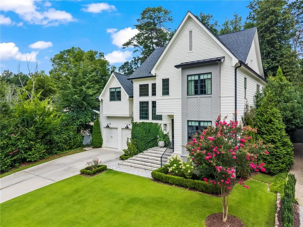 Contemporary architectural design featuring white siding, dark trim windows, a two-car garage, manicured landscaping, and a tiered stone walkway