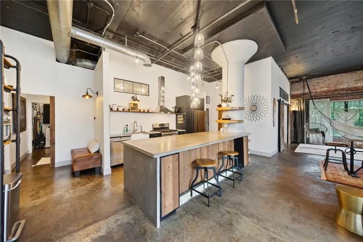 Polished concrete flooring, exposed brick wall, exposed ductwork ceiling, kitchen island with wood paneling, and stainless steel appliances