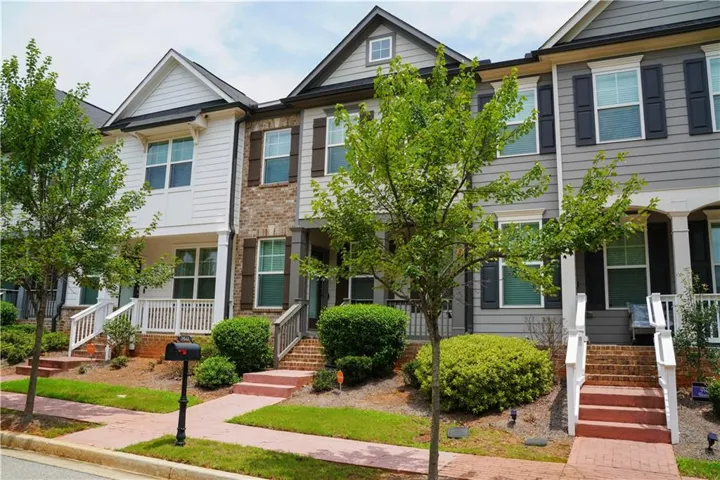 Modern townhome exterior featuring multi-level siding, brick accents, white trim, and dark window shutters