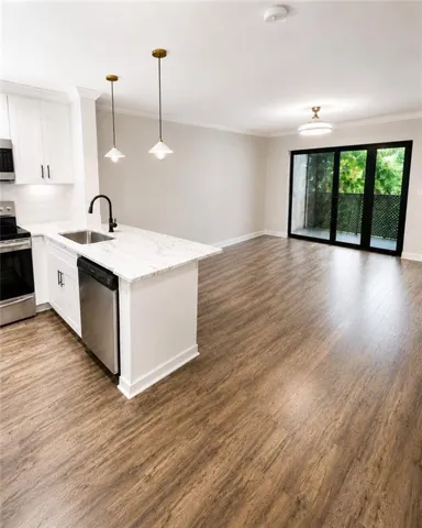 Open-concept living area featuring wood-finish flooring, a kitchen island with stone countertop, stainless steel appliances, white cabinetry, and a full-light glass door opening to a private balcony