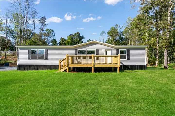Spacious manufactured home featuring a modern exterior with horizontal siding, multiple large windows, and a covered wooden deck with balustrade railing