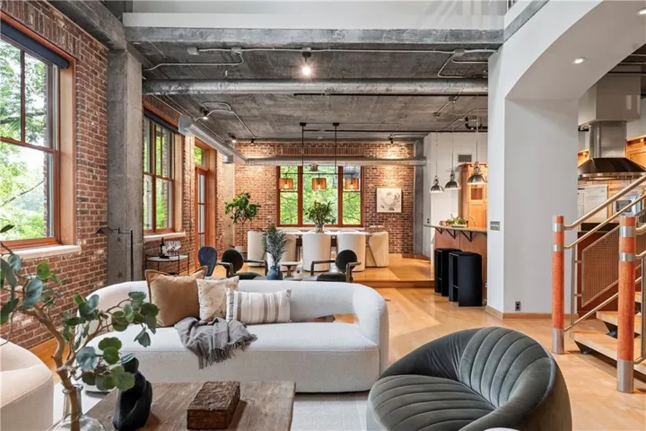 Open-concept living space with exposed brick walls, wood-finish flooring, and a concrete ceiling featuring exposed conduit