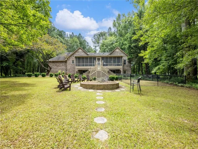 Spacious backyard featuring a brick exterior, two-story screened porch, a stone fire pit, and a fenced area
