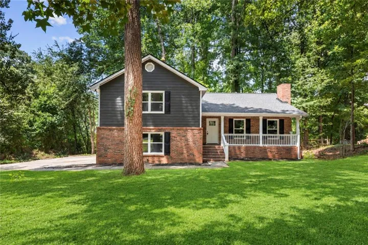Two-story residence featuring a brick and siding exterior, a covered front porch with white railing, a prominent brick chimney, and a gravel driveway