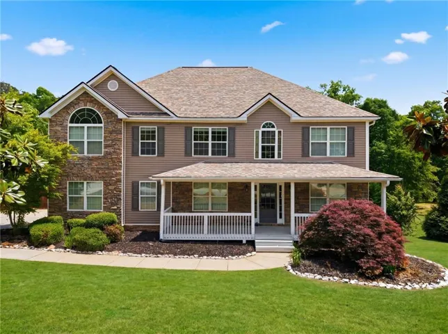 Two-story residence featuring a covered front porch with white railings, stone and siding exterior, and an arched window
