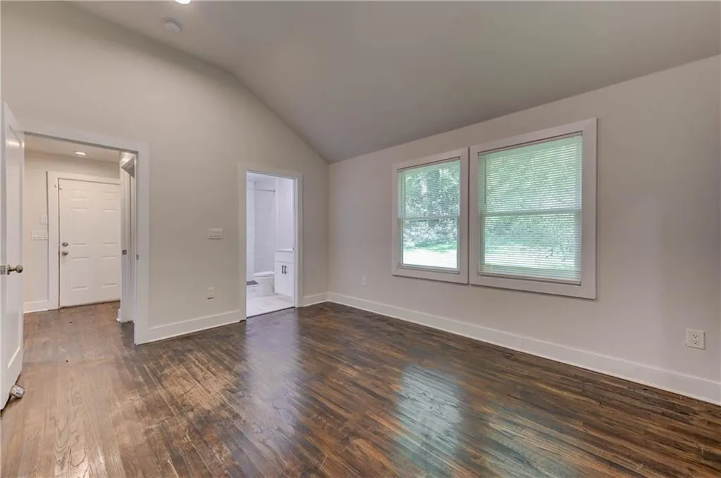 Unfurnished bedroom with vaulted ceiling, dark wood finished floors, and connected bathroom