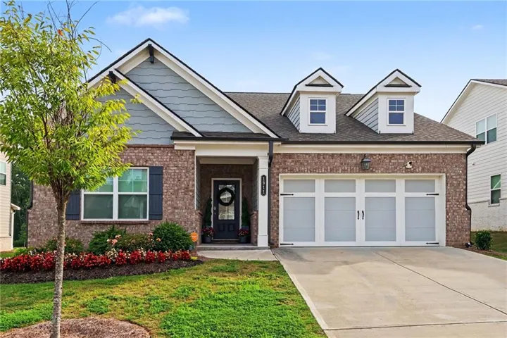 Brick facade residence featuring a covered front entry, twin garage doors with decorative hardware, two dormer windows, and a landscaped front yard