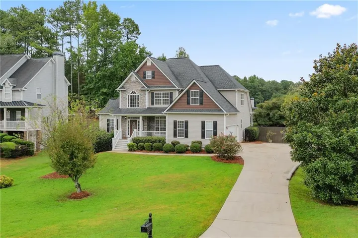 Two-story residence featuring a stone and siding facade, a covered front porch with white railings, a dark shingle roof, and a paved driveway