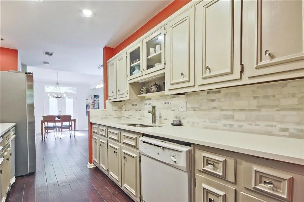 Kitchen with dark hardwood / wood-style floors, stainless steel fridge, backsplash, white dishwasher, and sink