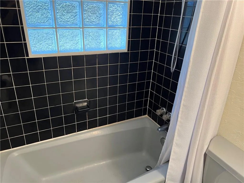 Bathroom with shower / bathtub combination with curtain and a textured wall