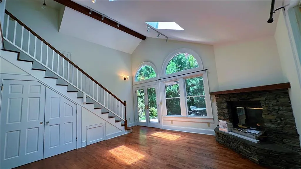Unfurnished living room with track lighting, a skylight, stairs, wood finished floors, and a stone fireplace