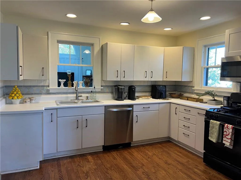 Kitchen featuring stainless steel appliances, backsplash, light countertops, pendant lighting, and dark wood-type flooring