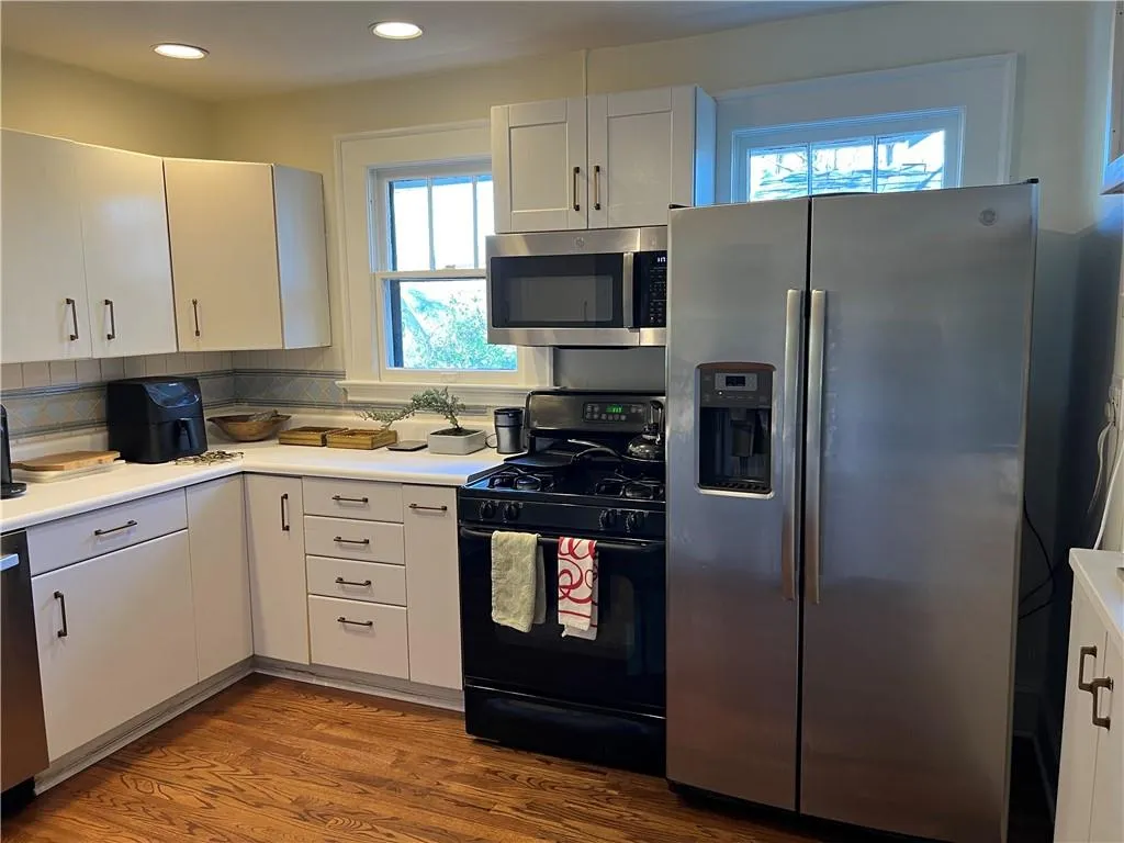 Kitchen featuring appliances with stainless steel finishes, wood finished floors, decorative backsplash, light countertops, and white cabinets