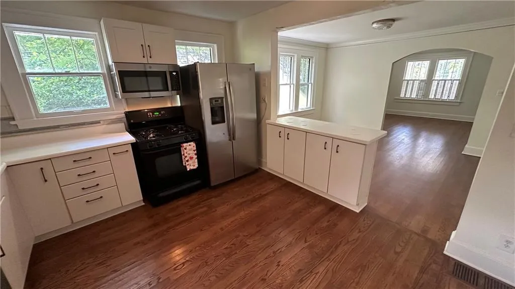 Kitchen with stainless steel appliances, a peninsula, dark wood-type flooring, white cabinets, and light countertops