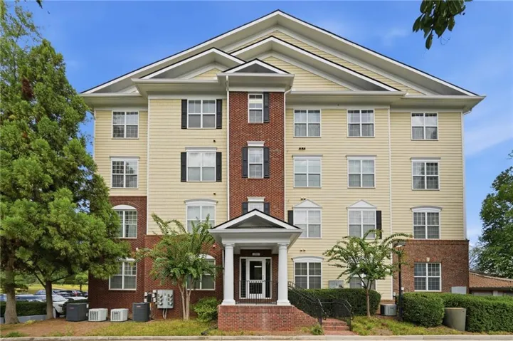Multi-story building featuring brick and siding facade, multiple windows with dark shutters, prominent gabled roofline, and a covered entry porch