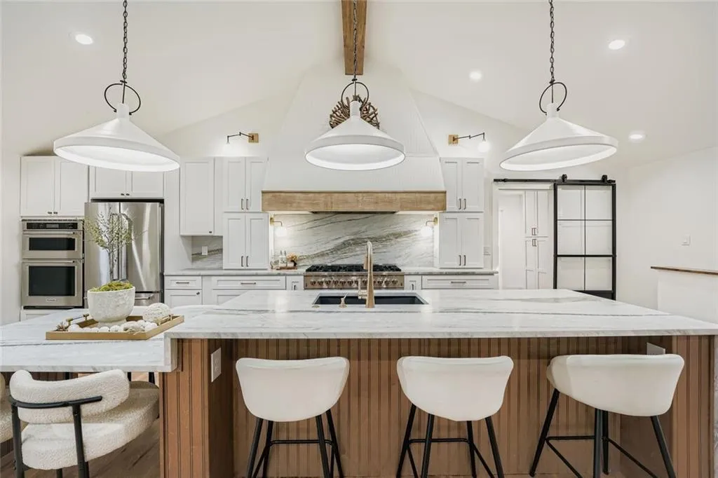 Kitchen with a barn door, white cabinets, pendant lighting, decorative backsplash, and appliances with stainless steel finishes