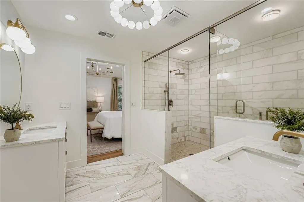 Ensuite bathroom with a chandelier, two vanities, light marble finish flooring, and a stall shower