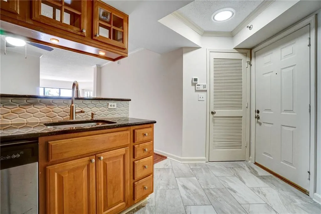 Kitchen featuring brown cabinets, dark stone countertops, ornamental molding, tasteful backsplash, and dishwasher