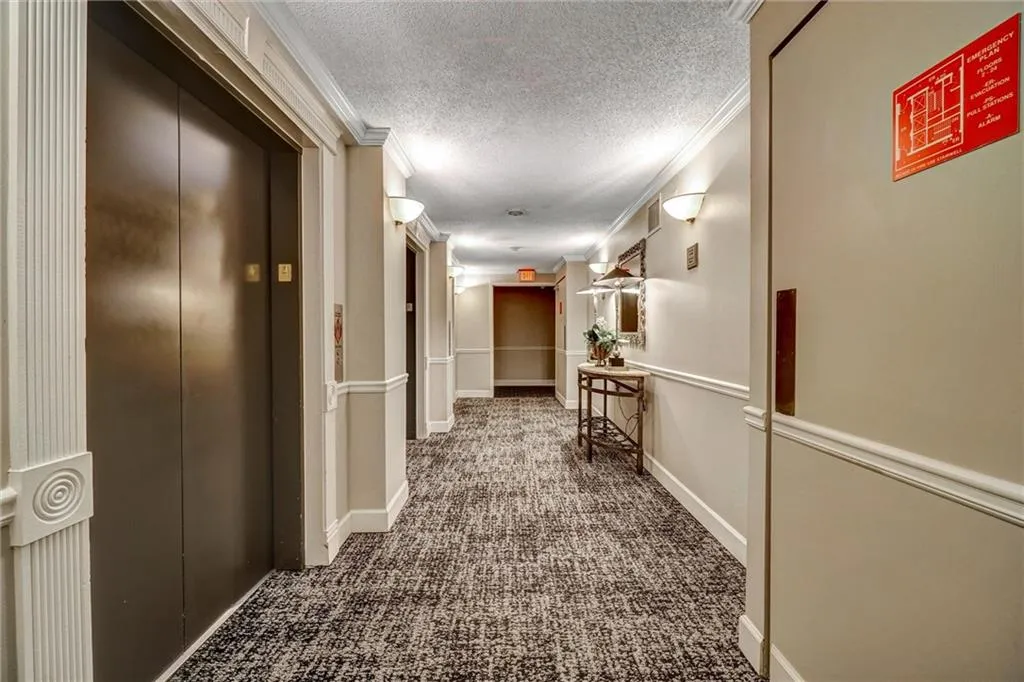 Hallway featuring dark colored carpet, a textured ceiling, elevator, and ornamental molding