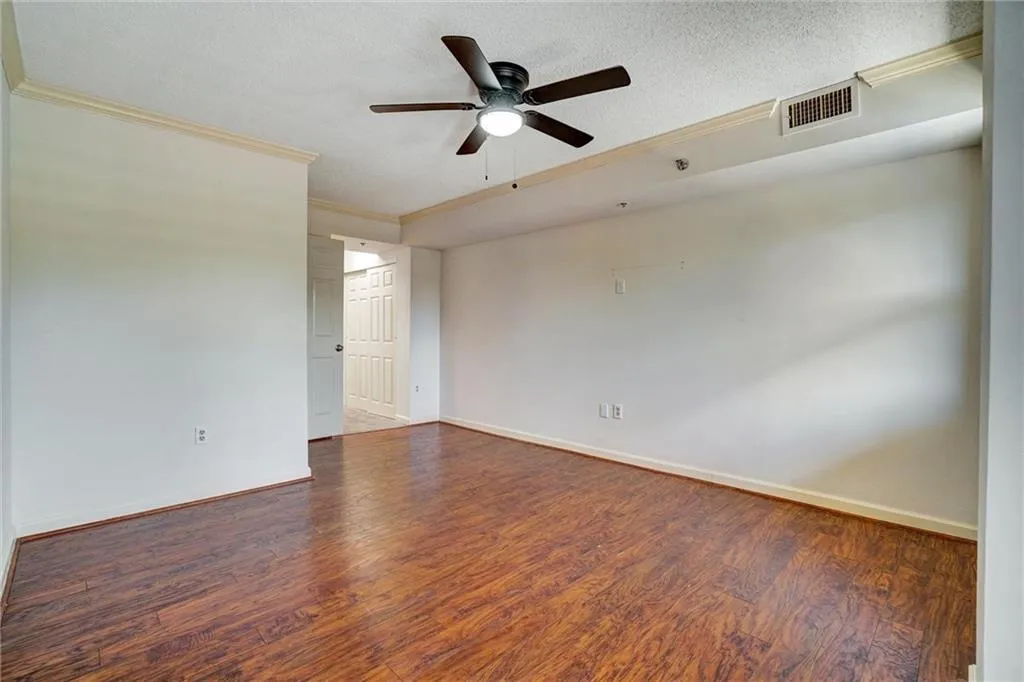 Empty room featuring dark wood-style floors, a textured ceiling, ornamental molding, and ceiling fan