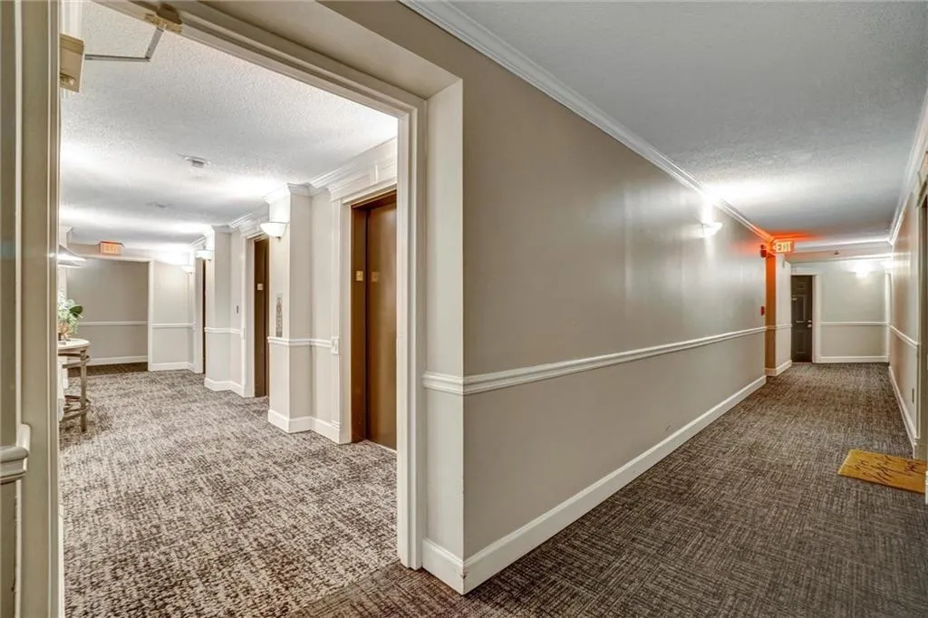 Hallway featuring a textured ceiling, dark carpet, crown molding, and elevator