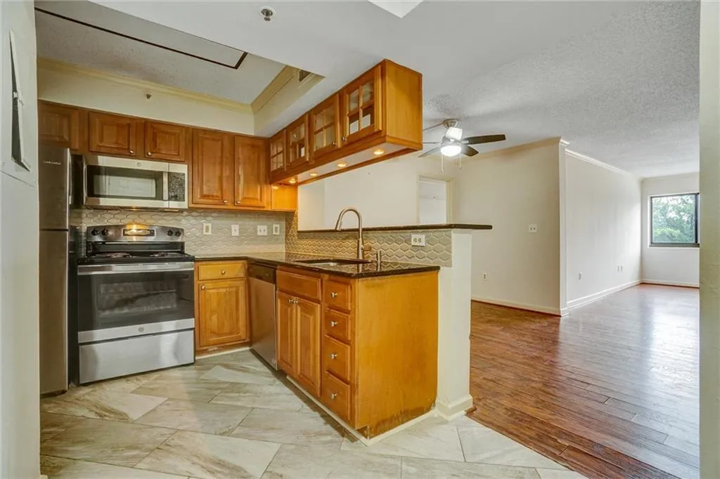 Kitchen featuring ornamental molding, dark stone countertops, stainless steel appliances, brown cabinets, and decorative backsplash