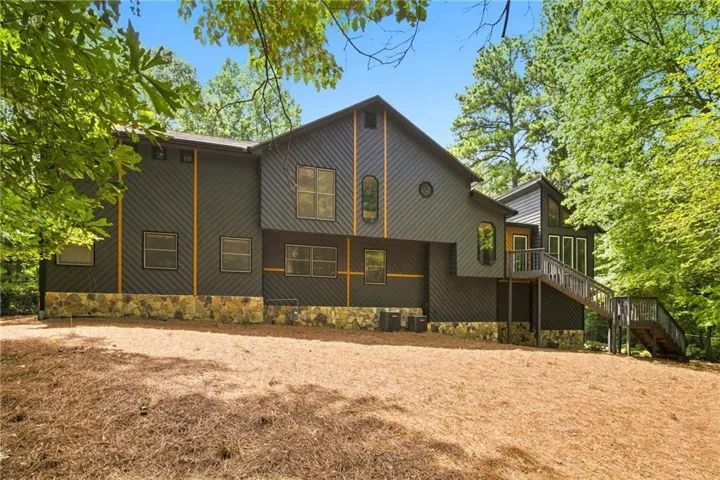 Dark-toned exterior siding with accent trim, stone foundation, multi-level wooden deck, and a sloping lot