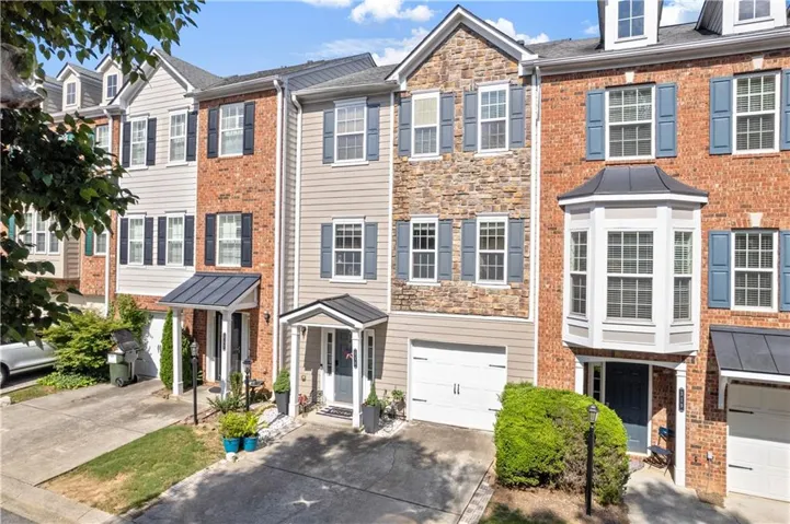 Townhome exterior featuring stone and siding facade, covered entry, attached garage, and blue window shutters