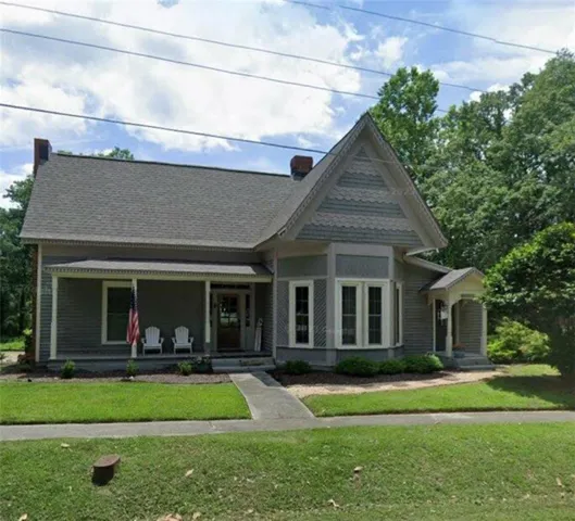 Victorian-style house featuring covered porch, a front lawn, roof with shingles, and a chimney