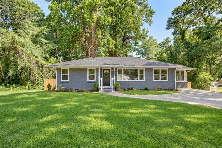Single-story residence featuring a gray exterior, white window trim, and a da, enhanced with greener grass and wreath on door.