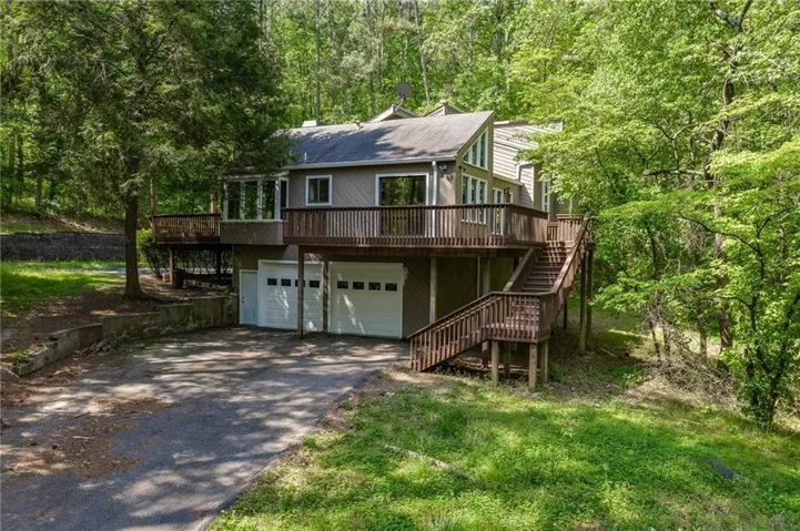 View of front of home featuring a deck, driveway, an attached garage, and a front lawn