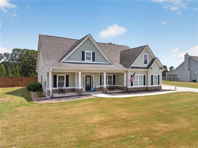 Traditional-style home featuring a covered front porch with column supports, multi-textured siding, dark shutters, and a paved driveway