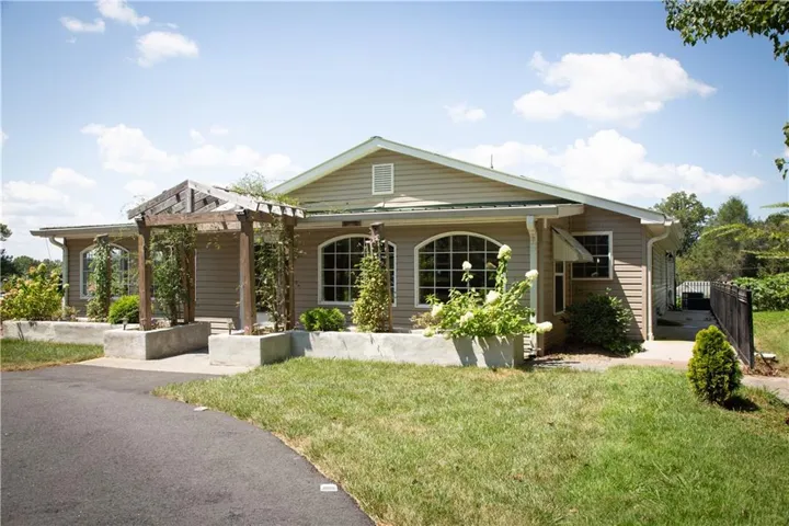 Siding exterior with arched grid windows, a wooden pergola, and concrete planters