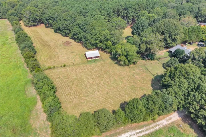 Expansive property featuring wooded perimeter, open clearings, and a red barn structure