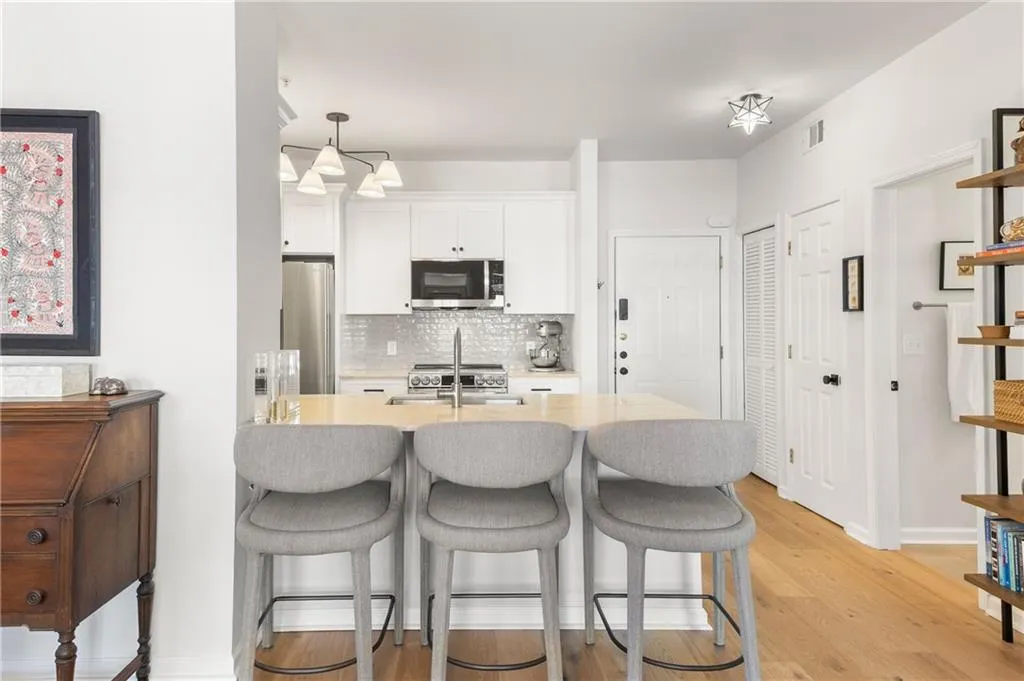 Kitchen with tasteful backsplash, a kitchen breakfast bar, light wood finished floors, appliances with stainless steel finishes, and white cabinetry