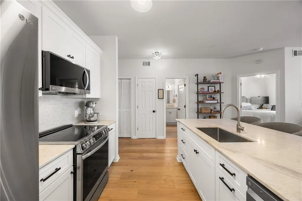 Kitchen featuring appliances with stainless steel finishes, white cabinetry, light wood-type flooring, light stone counters, and backsplash