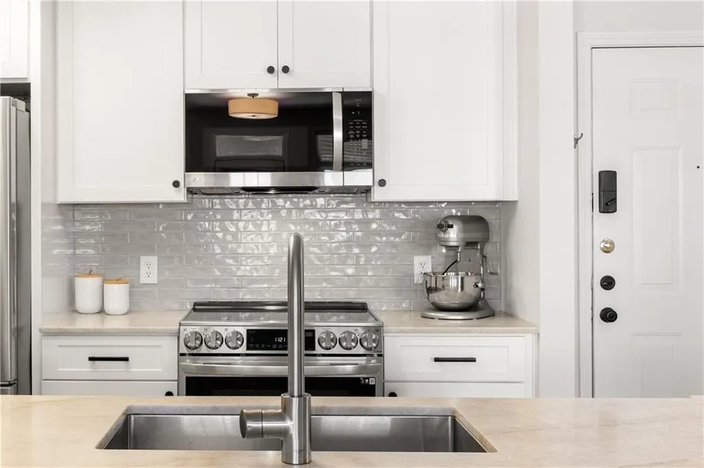Kitchen with appliances with stainless steel finishes, light countertops, tasteful backsplash, and white cabinets
