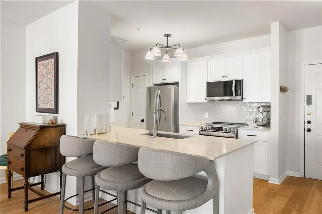 Kitchen with light wood finished floors, stainless steel appliances, a breakfast bar, white cabinetry, and light countertops