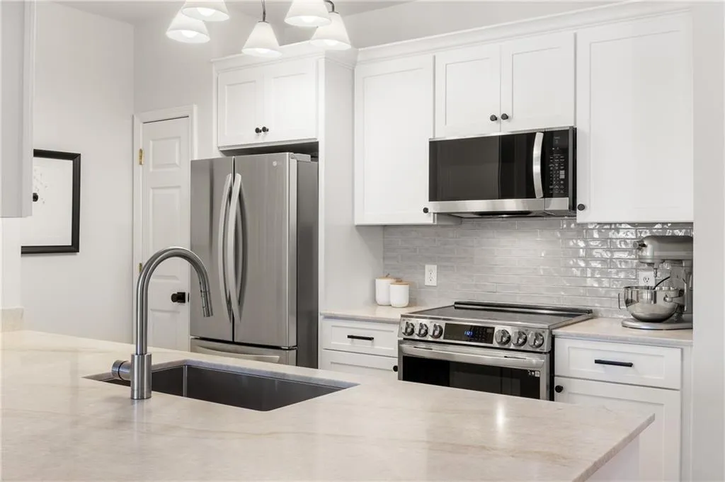Kitchen with appliances with stainless steel finishes, white cabinetry, decorative backsplash, light stone counters, and hanging light fixtures