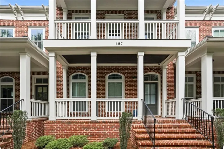 Brick facade with arched windows, multiple balconies featuring white railings, and a covered porch entry