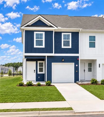 Contemporary townhome featuring a blue and white facade, an attached garage, a paved driveway, and manicured landscaping