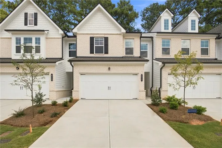 White brick exterior with black window shutters, dormer windows, and a two-car garage