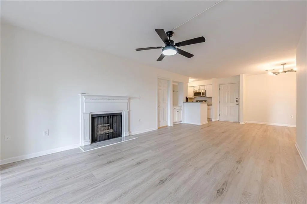 Unfurnished living room featuring light wood-style flooring, ceiling fan, and a fireplace with raised hearth